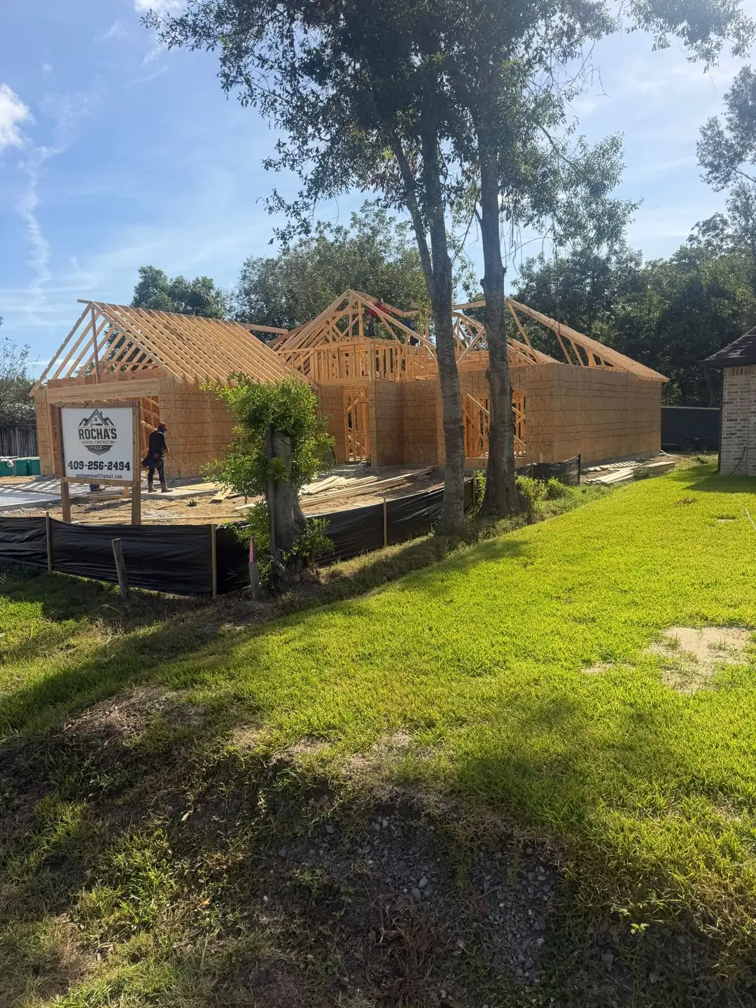 Wood framing + roof trusses going up, Rocha's sign on lot, Groves, TX