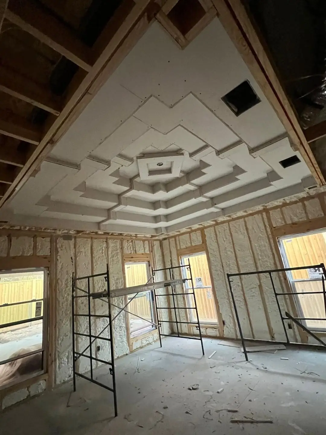 Framing -> spray foam -> drywall ceilings stages w/ workers on scaffold