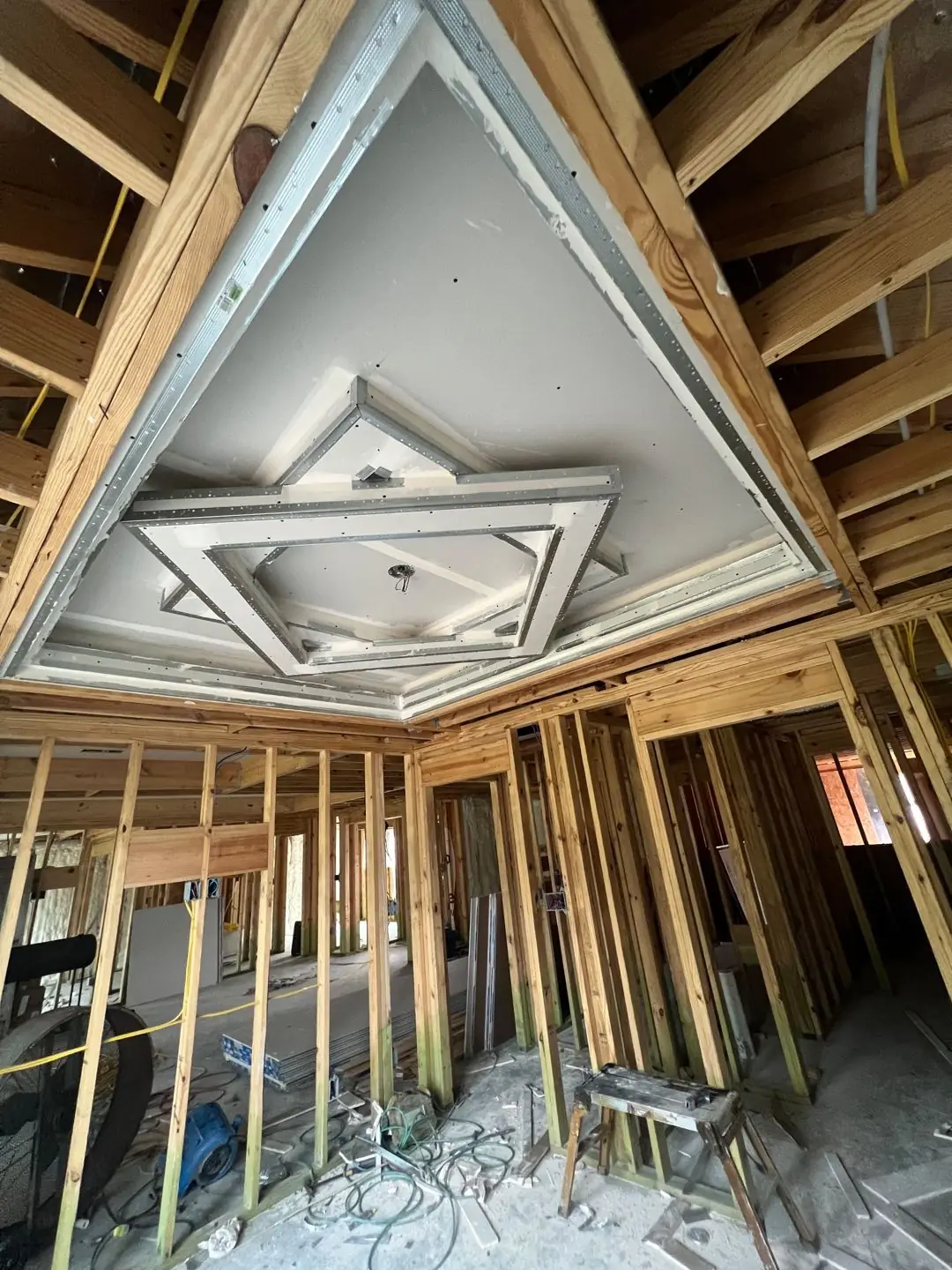 Framing / spray foam / insulation / drywall stages: tray ceilings, scaffold, workers, plumbing PEX manifold, electrical conduit