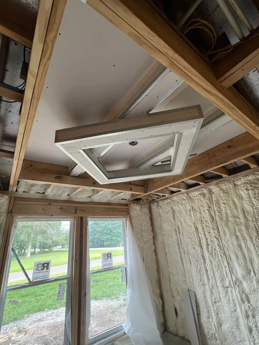 Framing / spray foam / insulation / drywall stages: tray ceilings, scaffold, workers, plumbing PEX manifold, electrical conduit