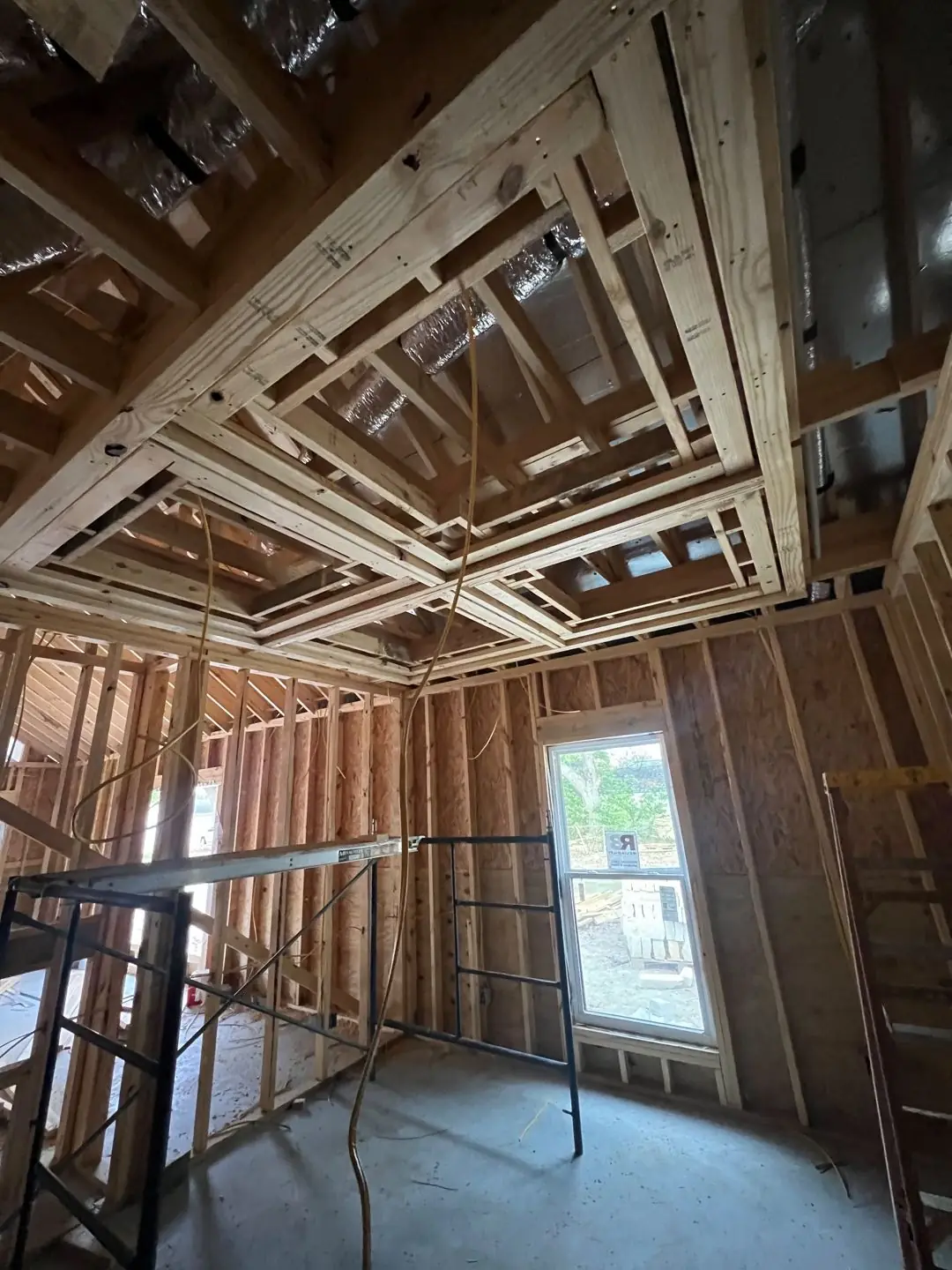 Framing / spray foam / insulation / drywall stages: tray ceilings, scaffold, workers, plumbing PEX manifold, electrical conduit