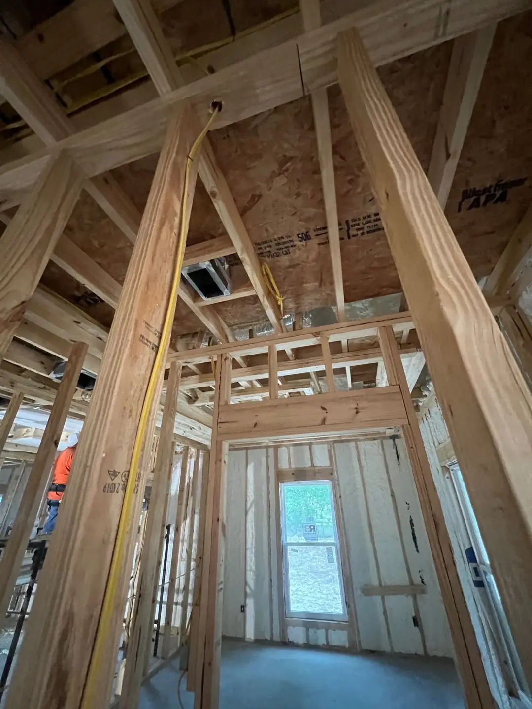 Framing / spray foam / insulation / drywall stages: tray ceilings, scaffold, workers, plumbing PEX manifold, electrical conduit