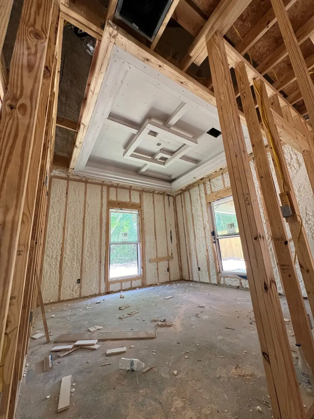 Framing / spray foam / insulation / drywall stages: tray ceilings, scaffold, workers, plumbing PEX manifold, electrical conduit