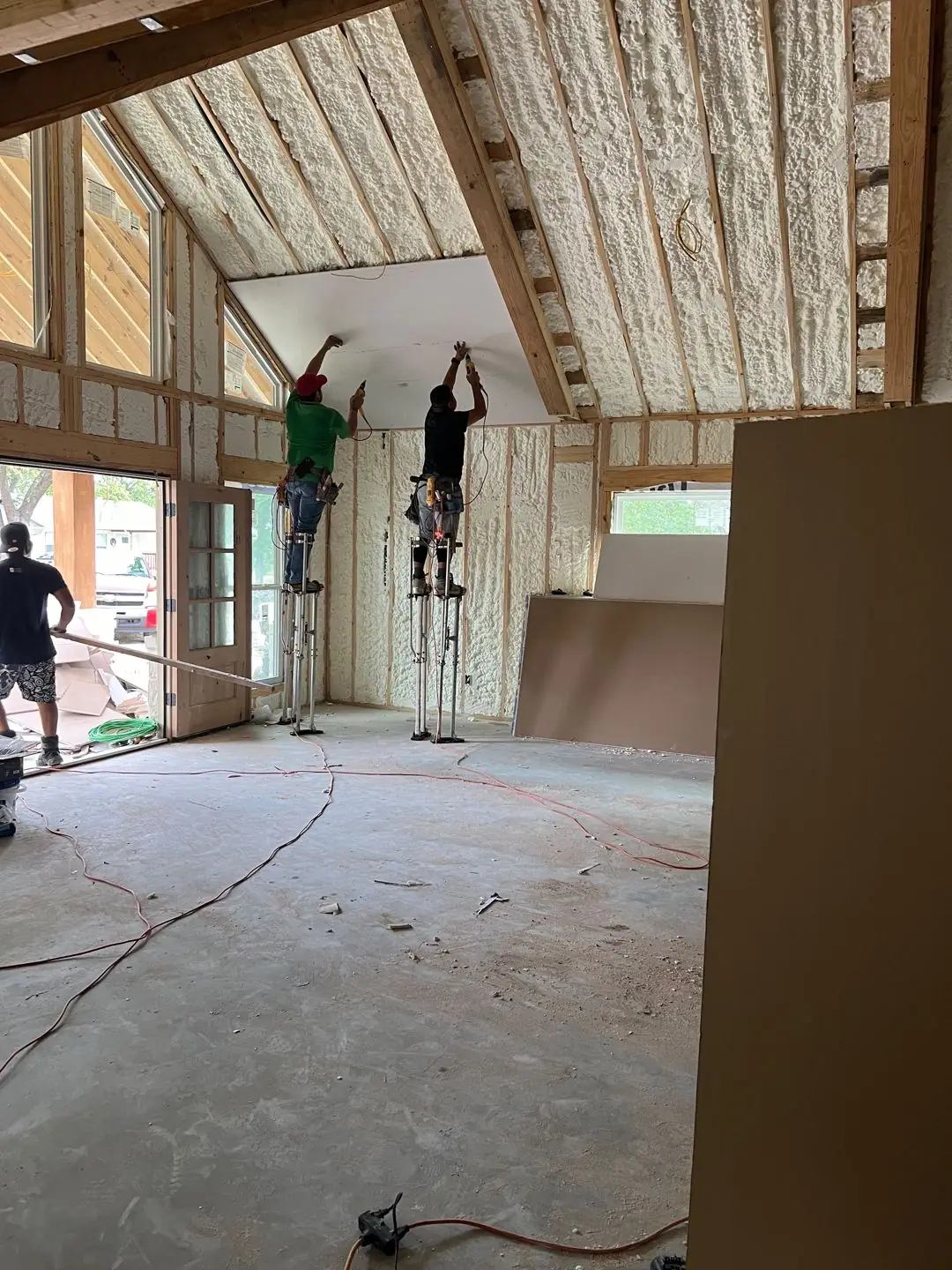 Framing / spray foam / insulation / drywall stages: tray ceilings, scaffold, workers, plumbing PEX manifold, electrical conduit