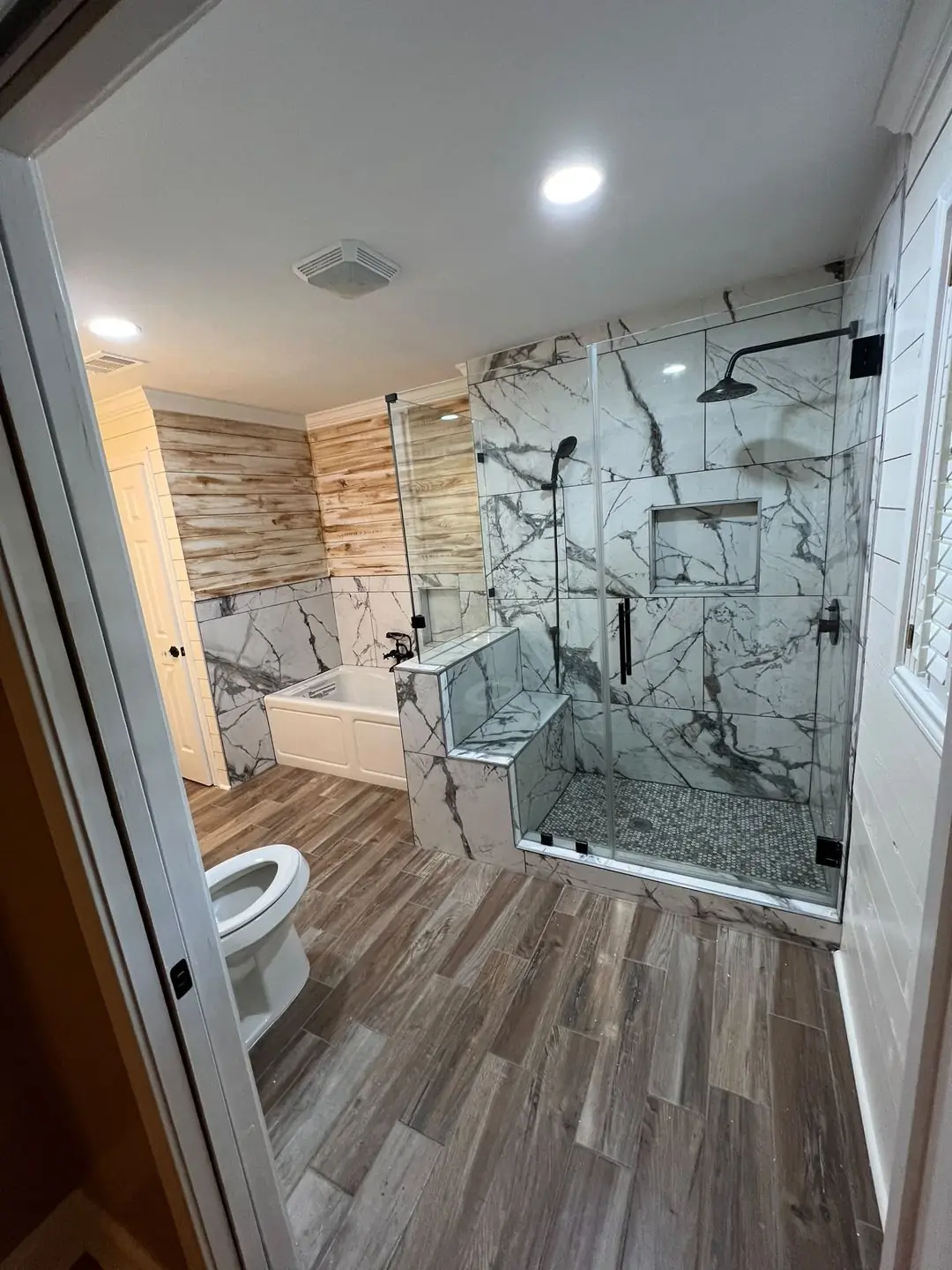 Finished primary bath: marble-look shower, wood accent wall, tub