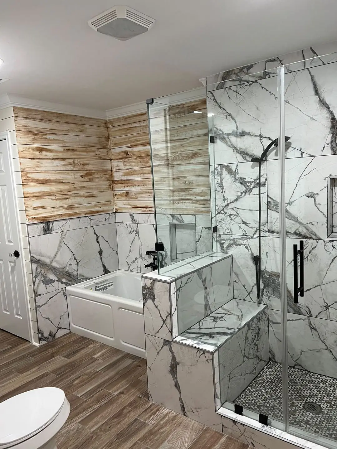 Finished primary bath: marble-look shower, wood accent wall, tub