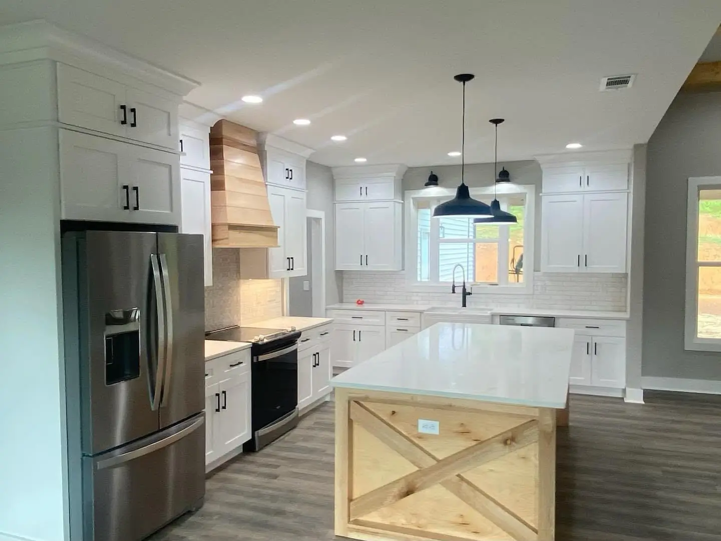Finished kitchen: white cabinets, X-barn-door island, quartz, pendants, wood range hood
