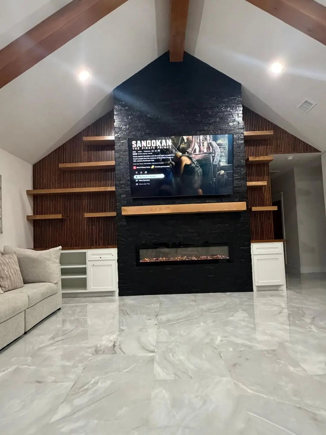 Finished living: dark stone fireplace wall, vaulted beams, TV